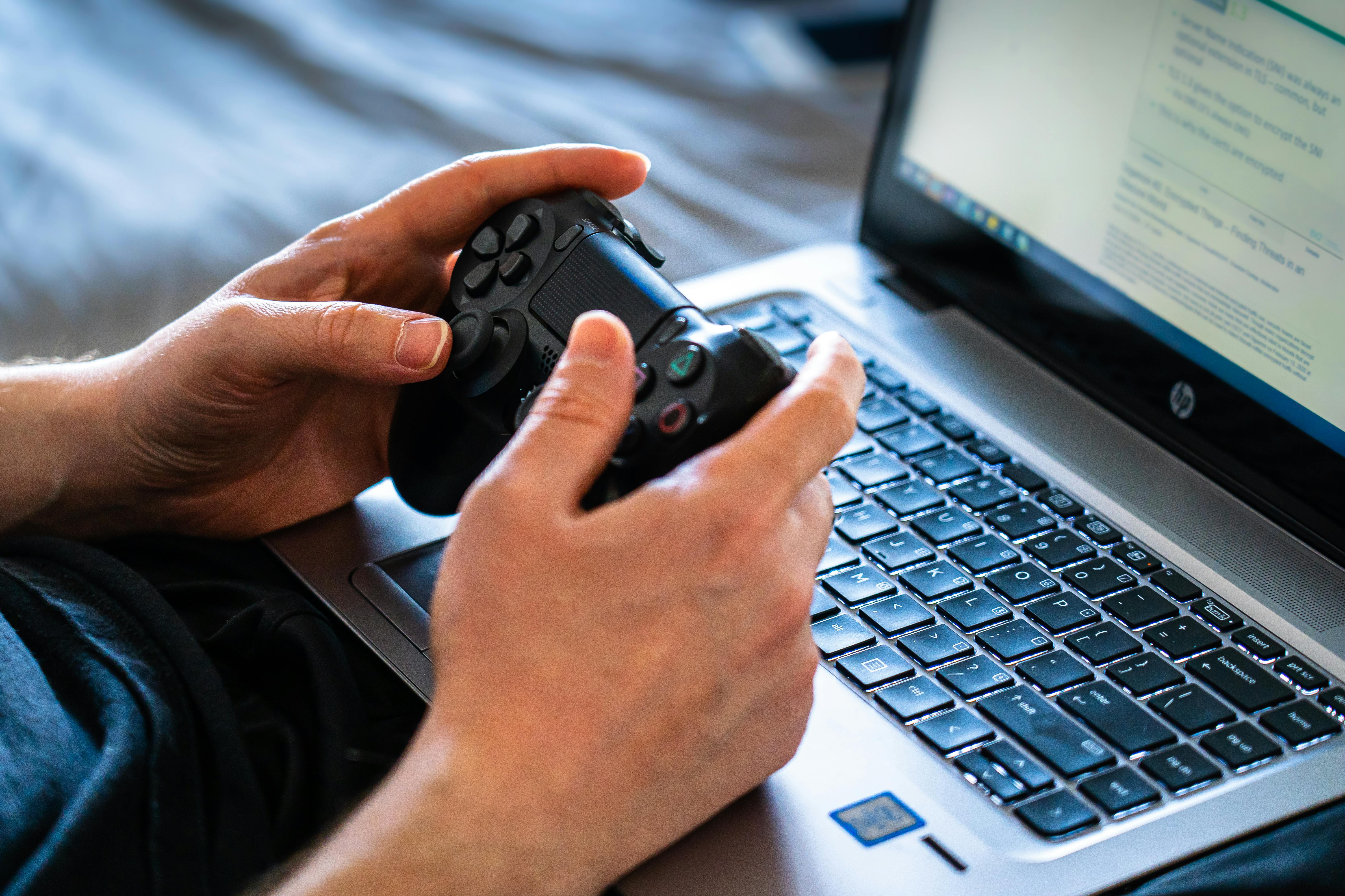 Person holds a gaming controller while interacting with a laptop, emphasizing modern gaming technology.